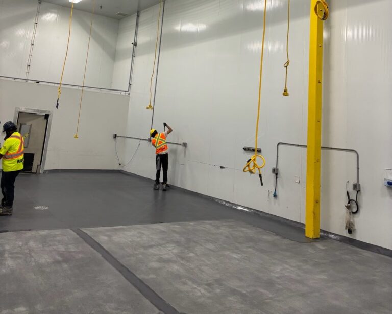 Team applies durable dark grey industrial resinous flooring in processing facility.