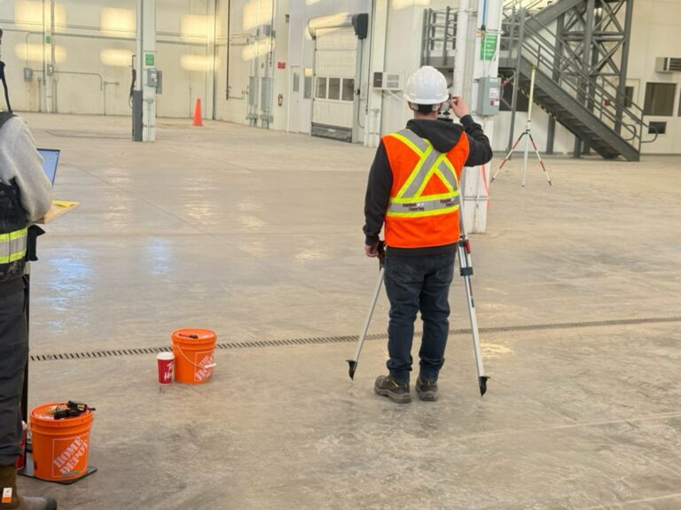 Applied Flooring worker surveying industrial concrete floor for leveling.