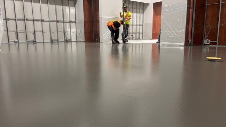 Industrial floor workers installing smooth gray epoxy coating on concrete.